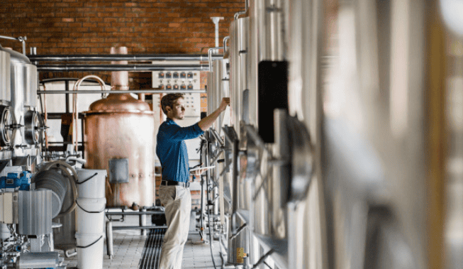 Brewer monitoring tanks inside a local craft brewery – insured by Crafted Insurance